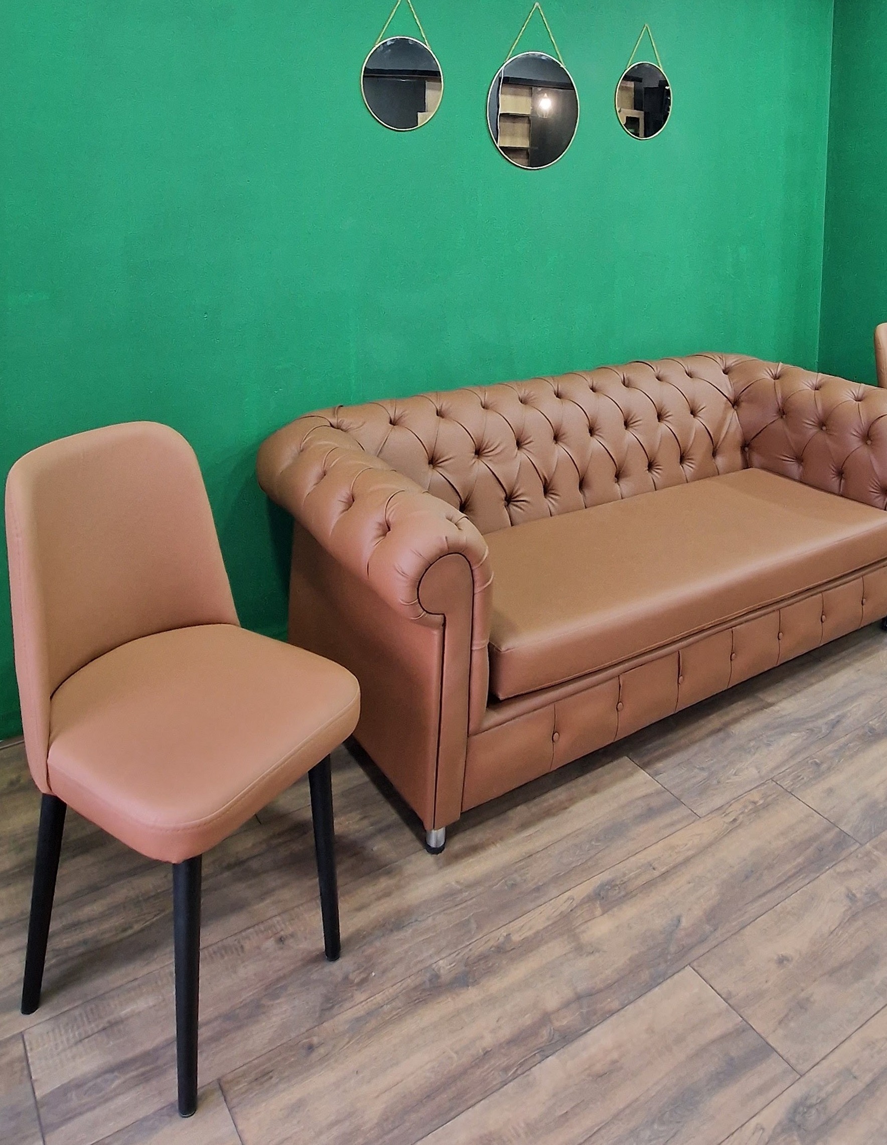 De wachthoek: een cognackleurige chesterfield en stoel voor de groene muur met drie ronde gouden spiegels