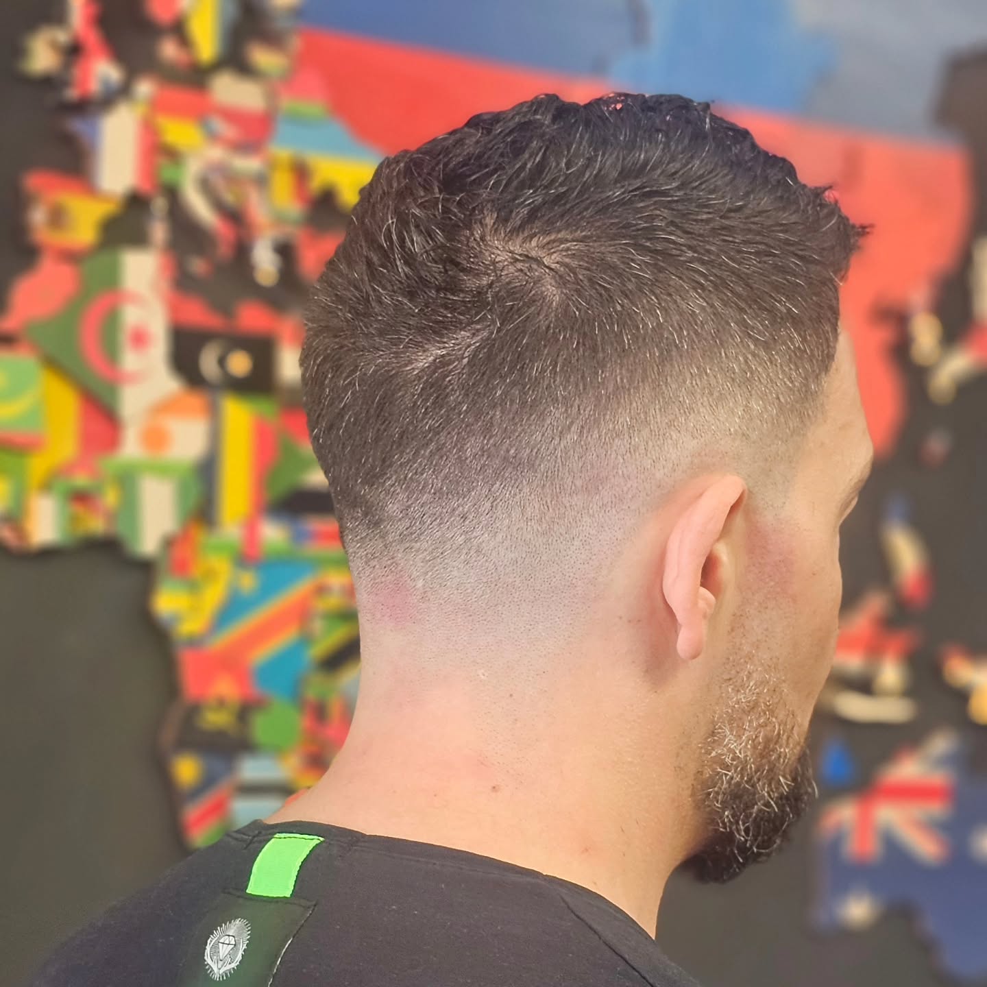 Skin fade met baard voor de muur met wereldvlaggen
